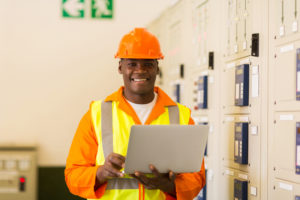 happy african electrical engineer with laptop computer in power plant control room